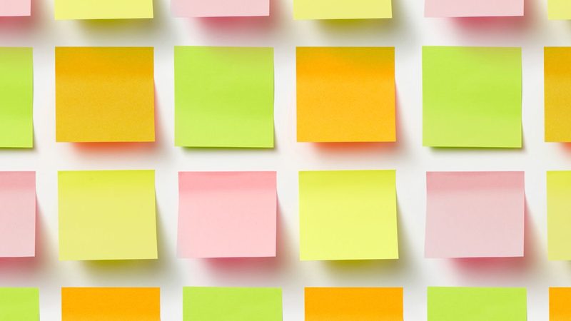 Rows of blank orange, green, yellow and pink sticky notes set out in a grid on a white wall