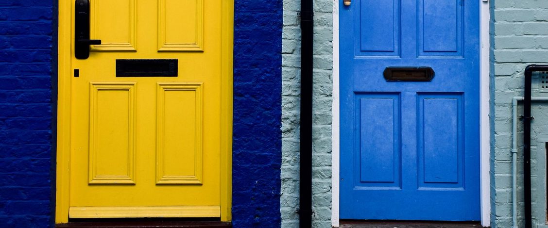 A yellow front door and a blue front door side by side in a London terrace, set in walls of dark blue and pale green brick